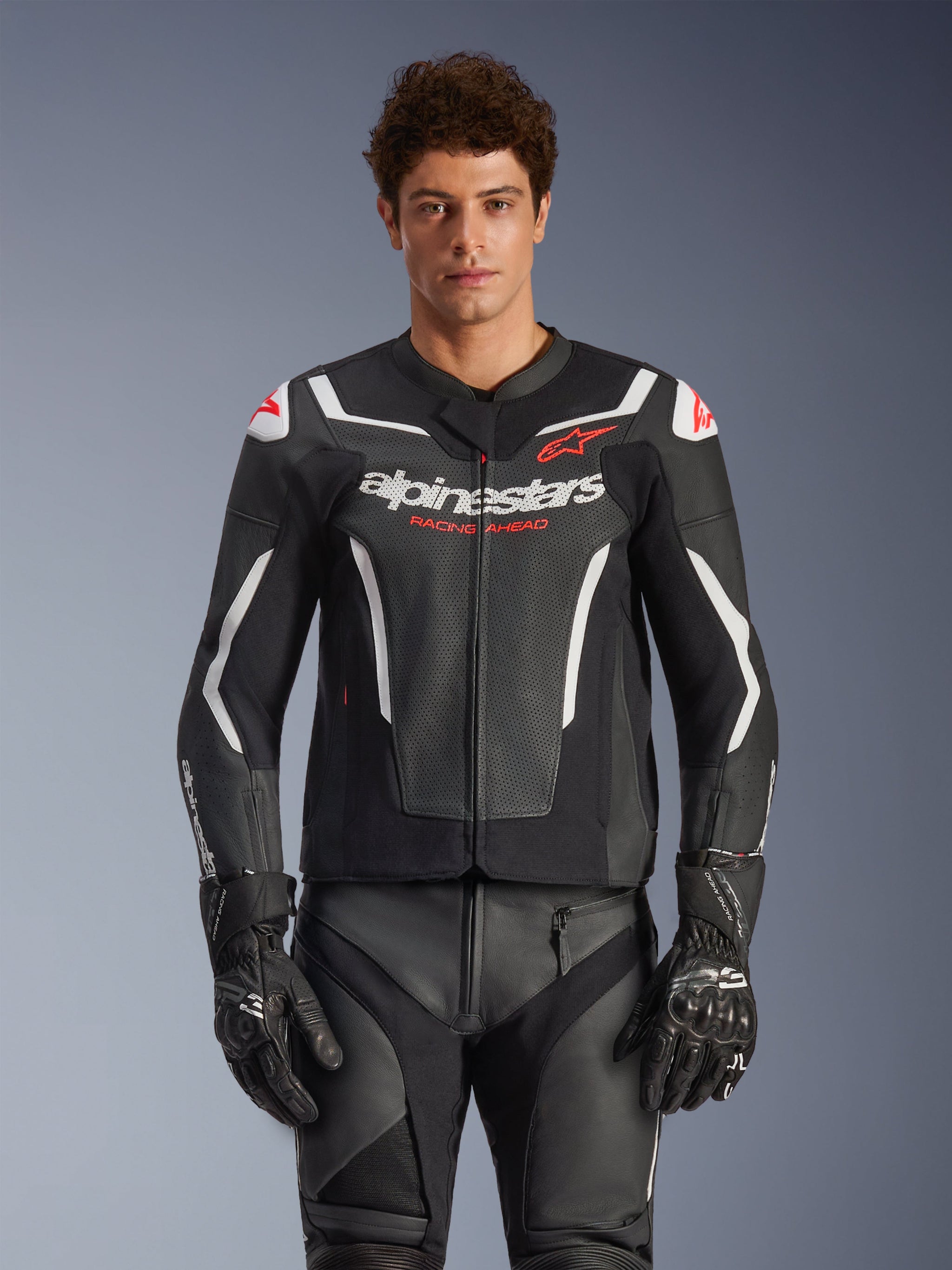 Alpinestars GP Force V2 Air Leather Jacket, Black with White and Red accents, model wearing perforated leather jacket with 'alpinestars' and 'RACING AHEAD' branding on the chest, paired with matching racing pants and gloves, premium sport motorcycle gear