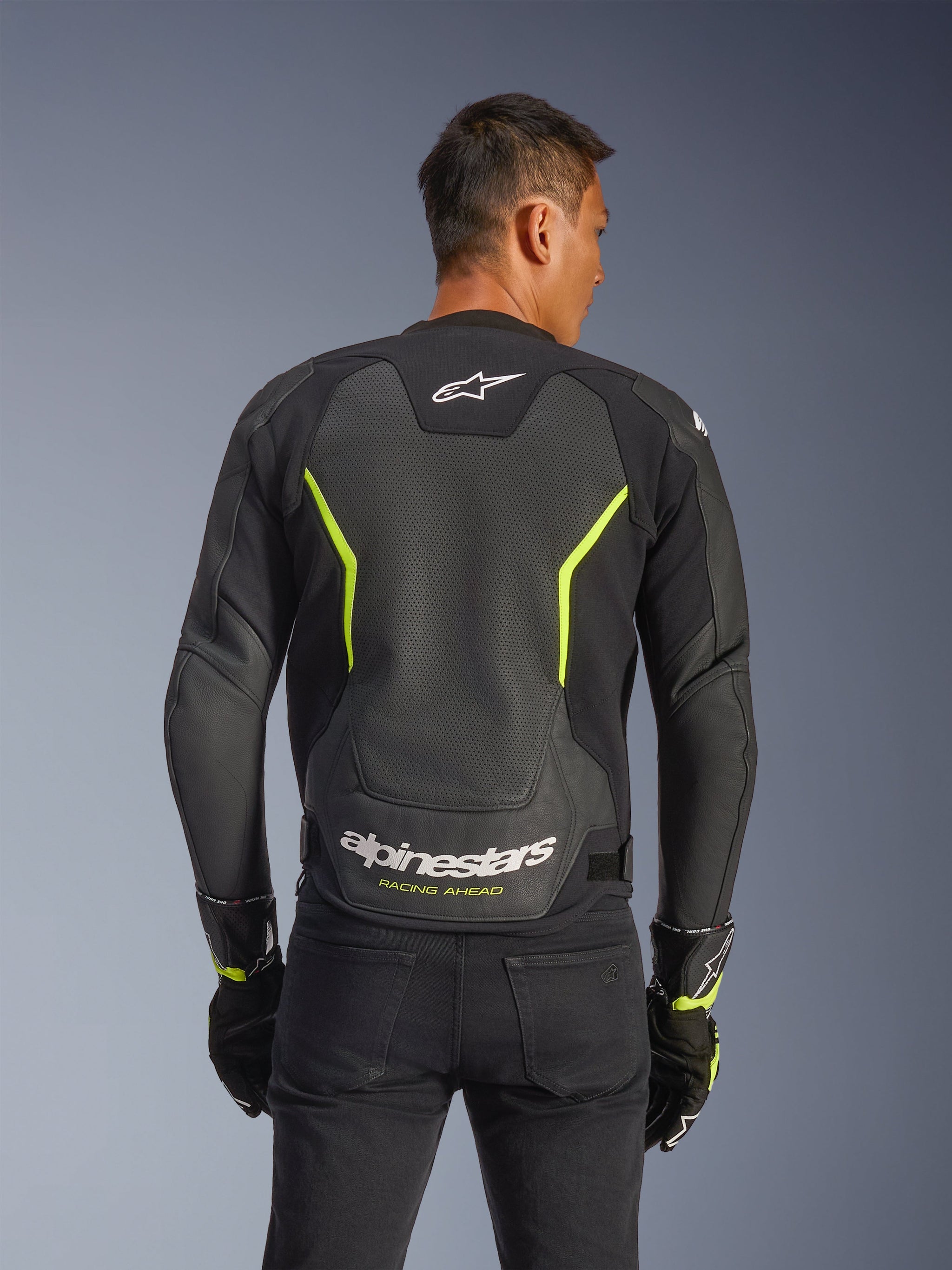 Alpinestars GP Force V2 Air Leather Jacket, Black and Yellow Fluo, back view of a male rider showing extensive perforated leather panels for airflow, white Alpinestars branding and yellow "Racing Ahead" text on the lower back, sport motorcycle gear for road riding.