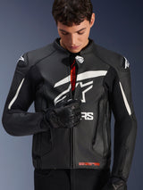 Alpinestars GP Plus V4 Leather Jacket, Black and White, male model zipping up the front to reveal red interior branding, featuring bold white Alpinestars logos on the chest and shoulders, worn with black leather motorcycle gloves, sport-derived leather riding apparel