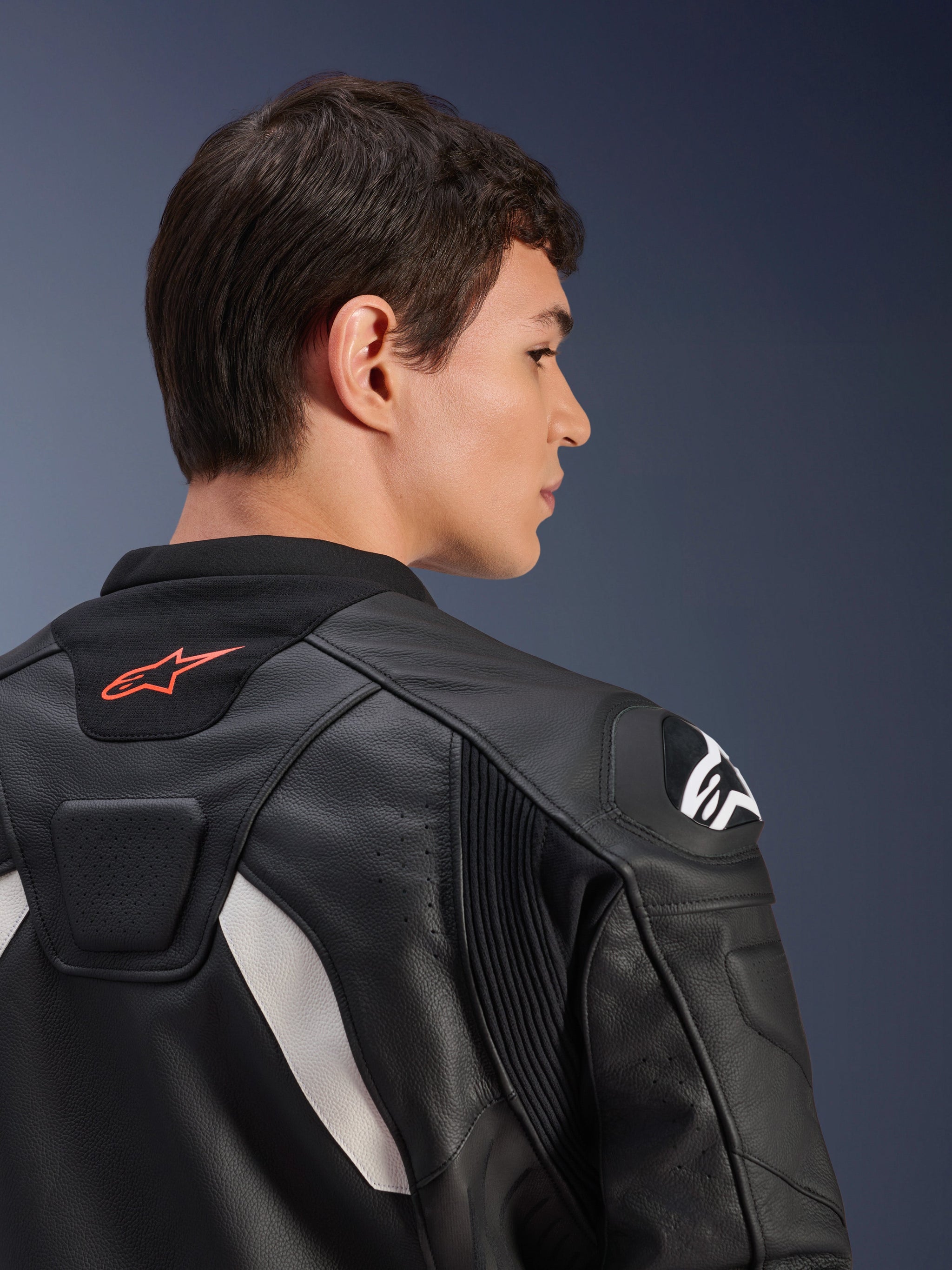 Alpinestars GP Plus V4 Leather Jacket, Black and White, close-up back view of a model wearing the jacket, featuring a red logo on the collar, white shoulder protectors, and durable leather construction with stretch panels