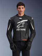Alpinestars GP Plus V4 Leather Jacket, Black with White accents, featuring a large white ASTARS logo and star graphic on the chest, worn with black motorcycle gloves and pants, sleek race-derived sport leather design