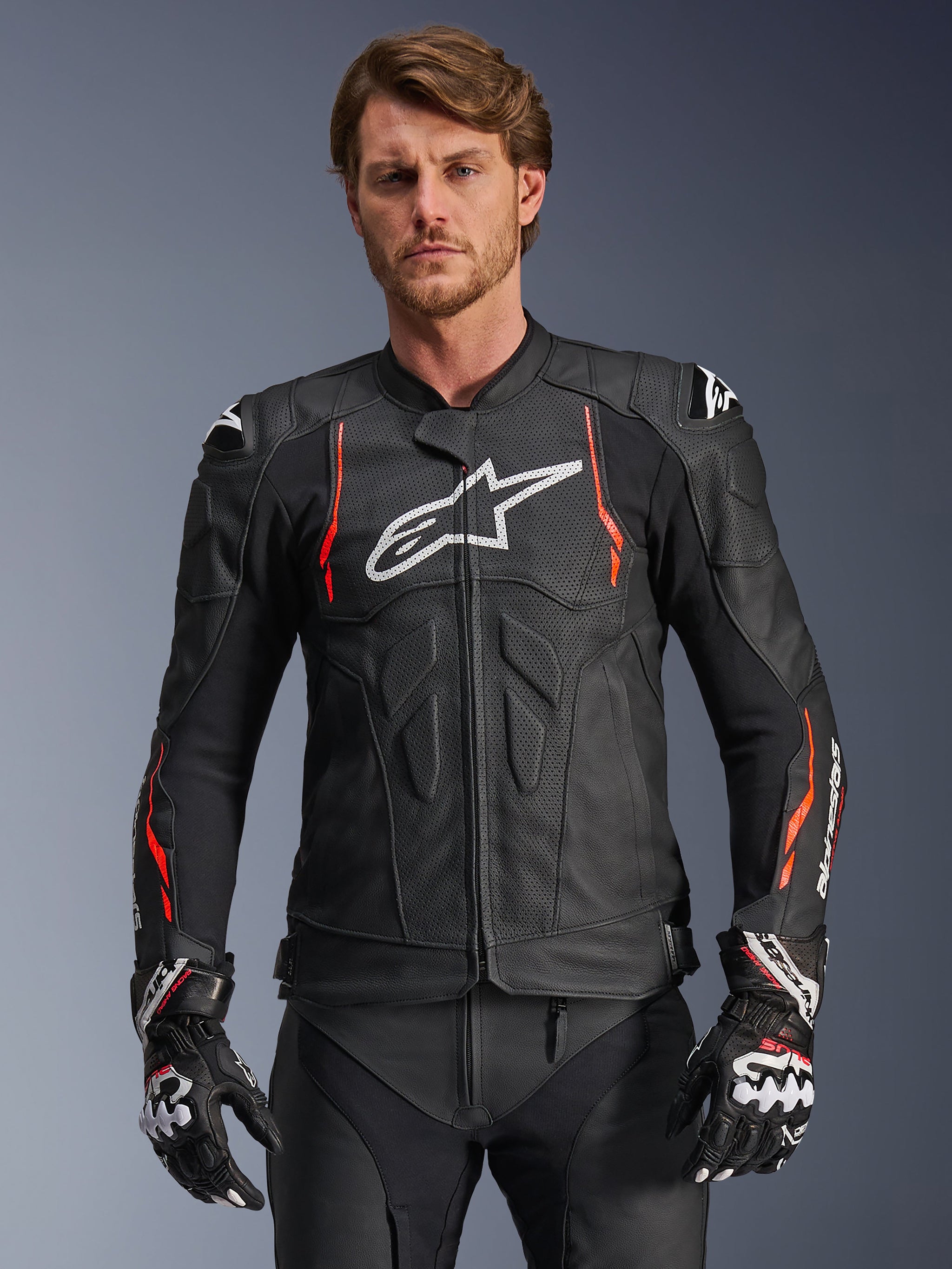 Alpinestars Dusk Airflow Leather Jacket, Black with Red Fluo and White accents, Leather Motorcycle Racing Jacket, featuring extensive perforations for ventilation, white chest logo, and external shoulder sliders, worn by a model with matching racing gloves