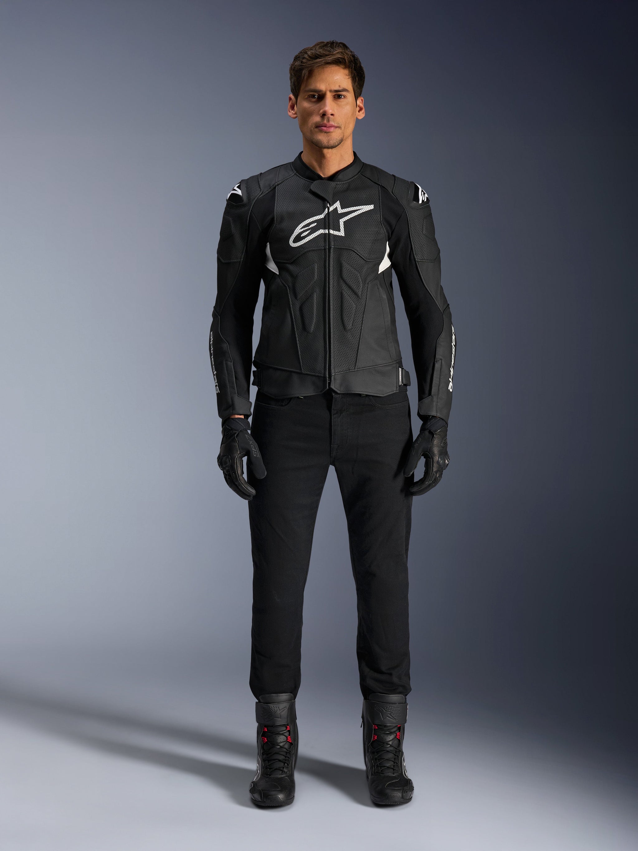 Alpinestars Dusk Airflow Leather Jacket, Black and White, motorcycle leather jacket with perforated panels for airflow, white Astars logo on chest, worn by a male rider with black pants, gloves, and riding boots, professional studio shot for sport motorcycle gear.