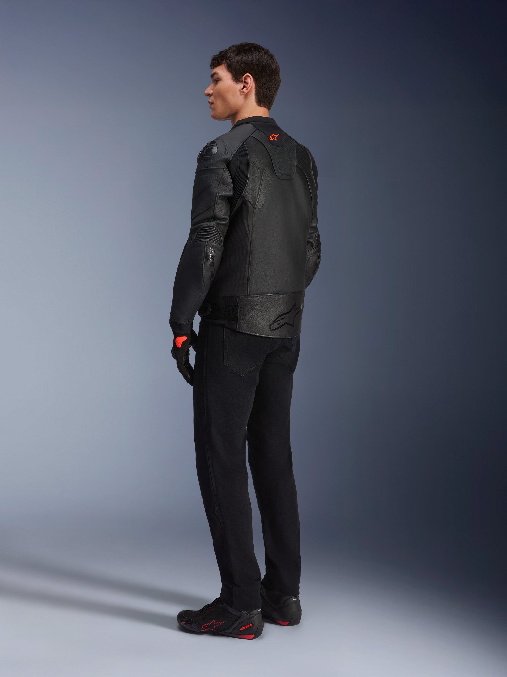 Alpinestars GP Plus R V4 Airflow Leather Jacket, Men's Sport Motorcycle Jacket, All Black, three-quarter rear view on a model, featuring perforated leather panels, red logo on the back, and integrated shoulder protection, worn with black pants and riding shoes
