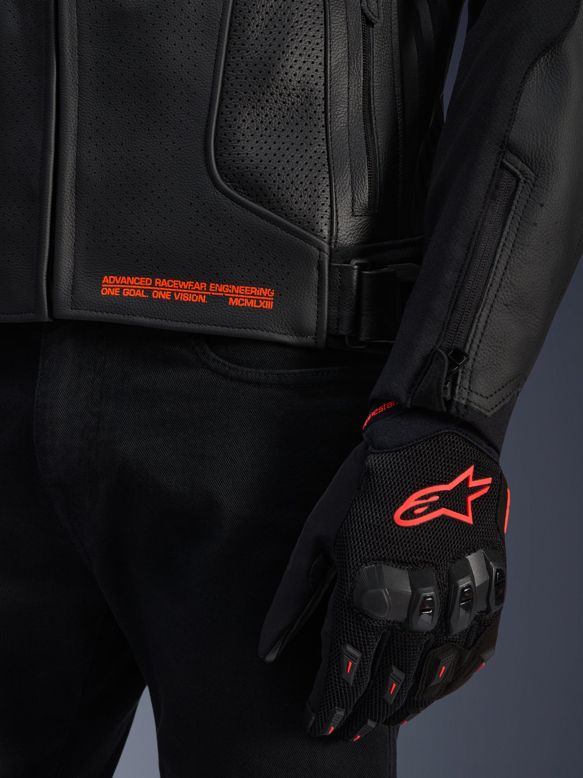 Alpinestars GP Plus R V4 Airflow Leather Jacket, close-up of black perforated leather with orange graphic text, paired with a black and orange motorcycle glove featuring the Astars logo