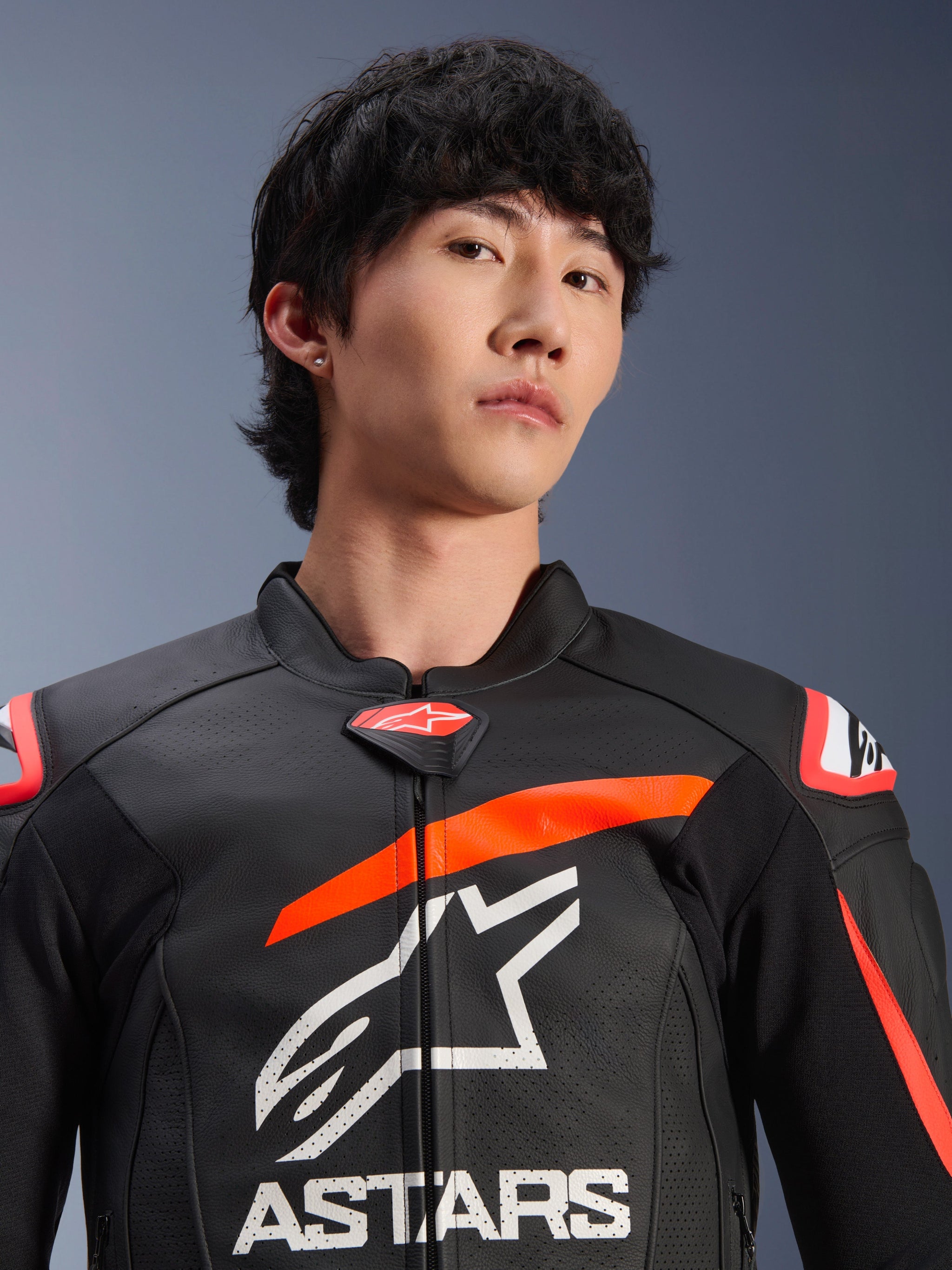 Alpinestars GP Plus R V4 Airflow Leather Jacket, Black with Red Fluo and White accents, worn by a man, featuring a prominent white Astars logo and branding on the chest, perforated leather panels for ventilation, and a high-performance racing-inspired design.