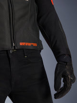 Alpinestars GP Plus R V4 Airflow Leather Jacket, close-up of waist and sleeve, black perforated leather with red fluo text branding reading 'Advanced Racewear Engineering', paired with black riding pants and SPX 7 motorcycle glove