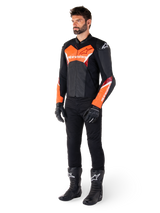 Male rider wearing the Alpinestars Faster V3 Leather Jacket in Black and Red Fluo, paired with black riding pants, gloves, and boots. The jacket features a race-derived silhouette with bold fluorescent red accents on the chest and sleeves, white Alpinestars branding, and a premium leather construction.