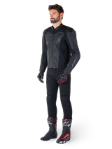 Man wearing Alpinestars Faster V3 Airflow Leather Jacket in Black Black, paired with black pants, black and red motorcycle gloves, and black racing boots with red and white accents, full-body sport riding gear