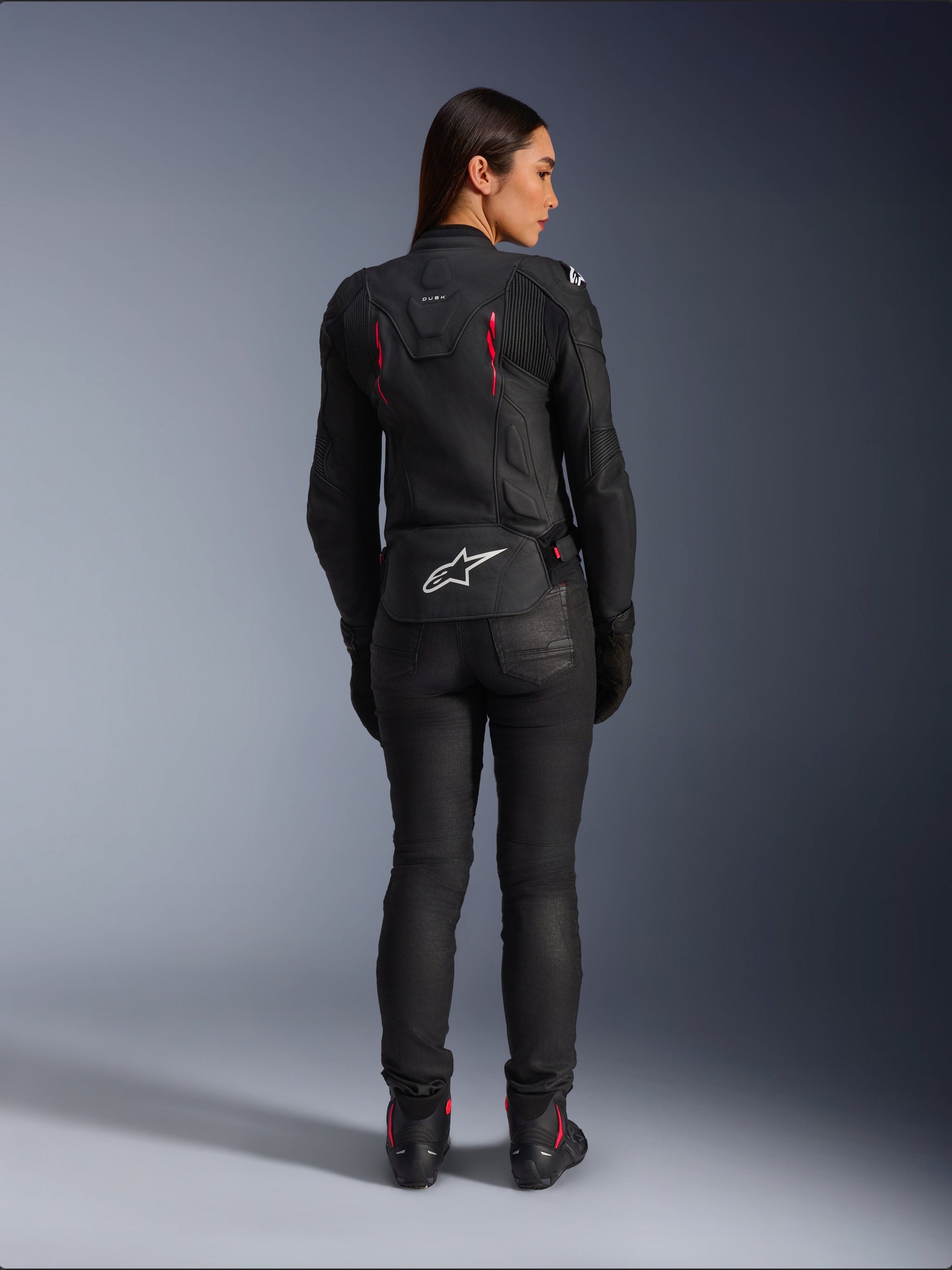 Alpinestars Stella Dusk Leather Jacket, rear view, black leather with Diva Pink and White accents, features white Alpinestars logo on lower back and pink vent details, worn with black riding pants and boots, premium sport motorcycle gear for women