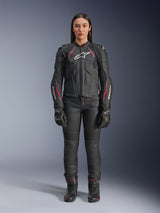 A woman wearing the Alpinestars Stella Dusk Leather Jacket in Black Diva Pink White, featuring a white chest logo and pink accents on the shoulders and sleeves, paired with black motorcycle pants, gloves, and boots.