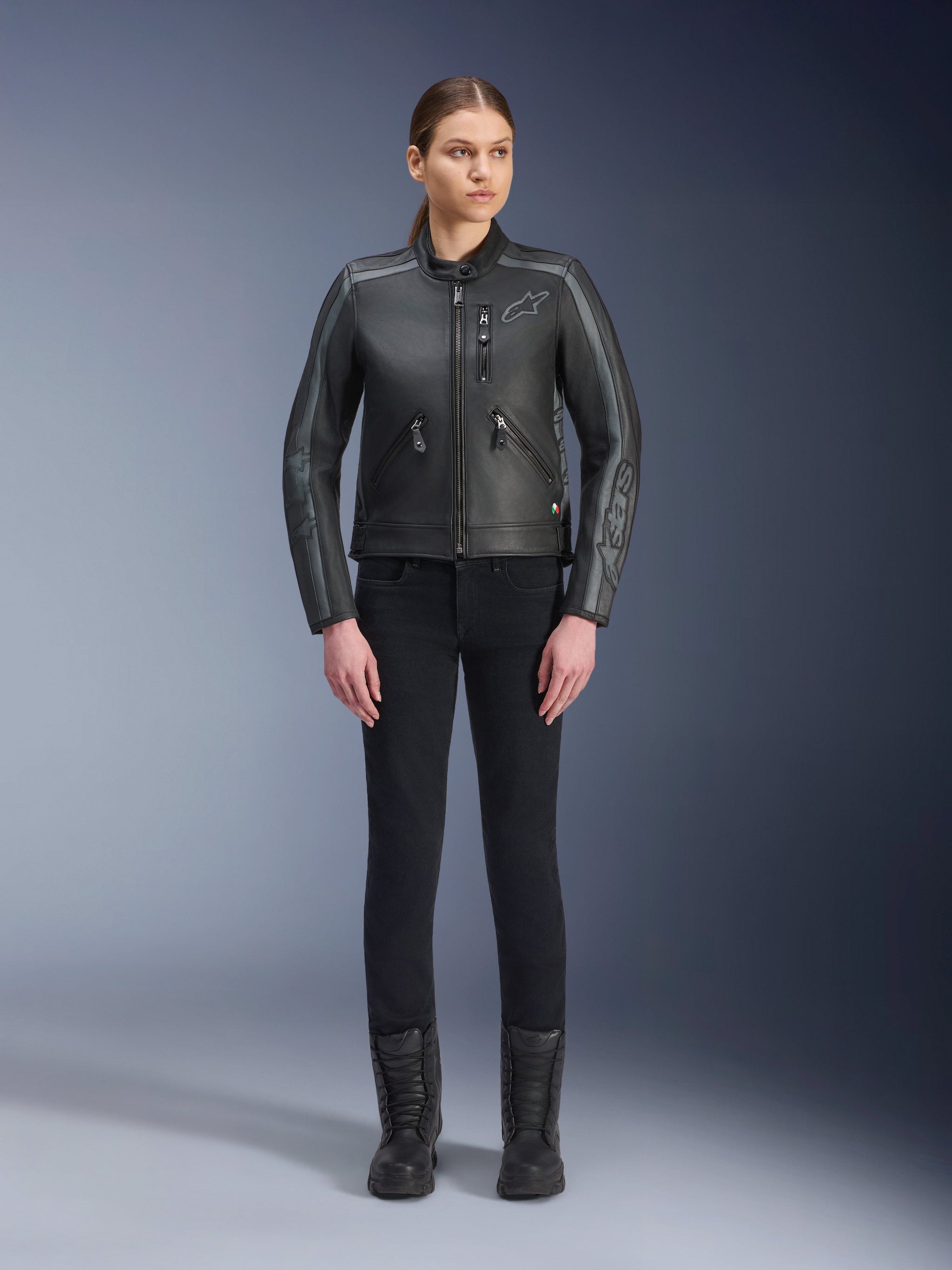 Alpinestars Stella Dyno Leather Jacket, Women's Motorcycle Jacket, Black Tar Gray Dark Gray, full-body studio view of a model wearing the jacket with black slim-fit pants and black boots, featuring bovine leather construction with gray accents and subtle Alpinestars branding on the chest and sleeves.