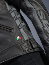 Alpinestars Stella Dyno Leather Jacket detail, Black and Tar Gray bovine leather, close-up featuring small Italian flag embroidery, adjustable waist buckle, and gray leather panels with embossed Alpinestars logos and Stella branding on the sleeve.