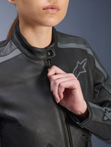 Alpinestars Stella Dyno Leather Jacket, close-up of front zipper and collar being adjusted by a model, Black with Tar Gray and Dark Gray accents, featuring the embroidered Alpinestars logo on the chest, premium bovine leather texture, urban motorcycle gear for women
