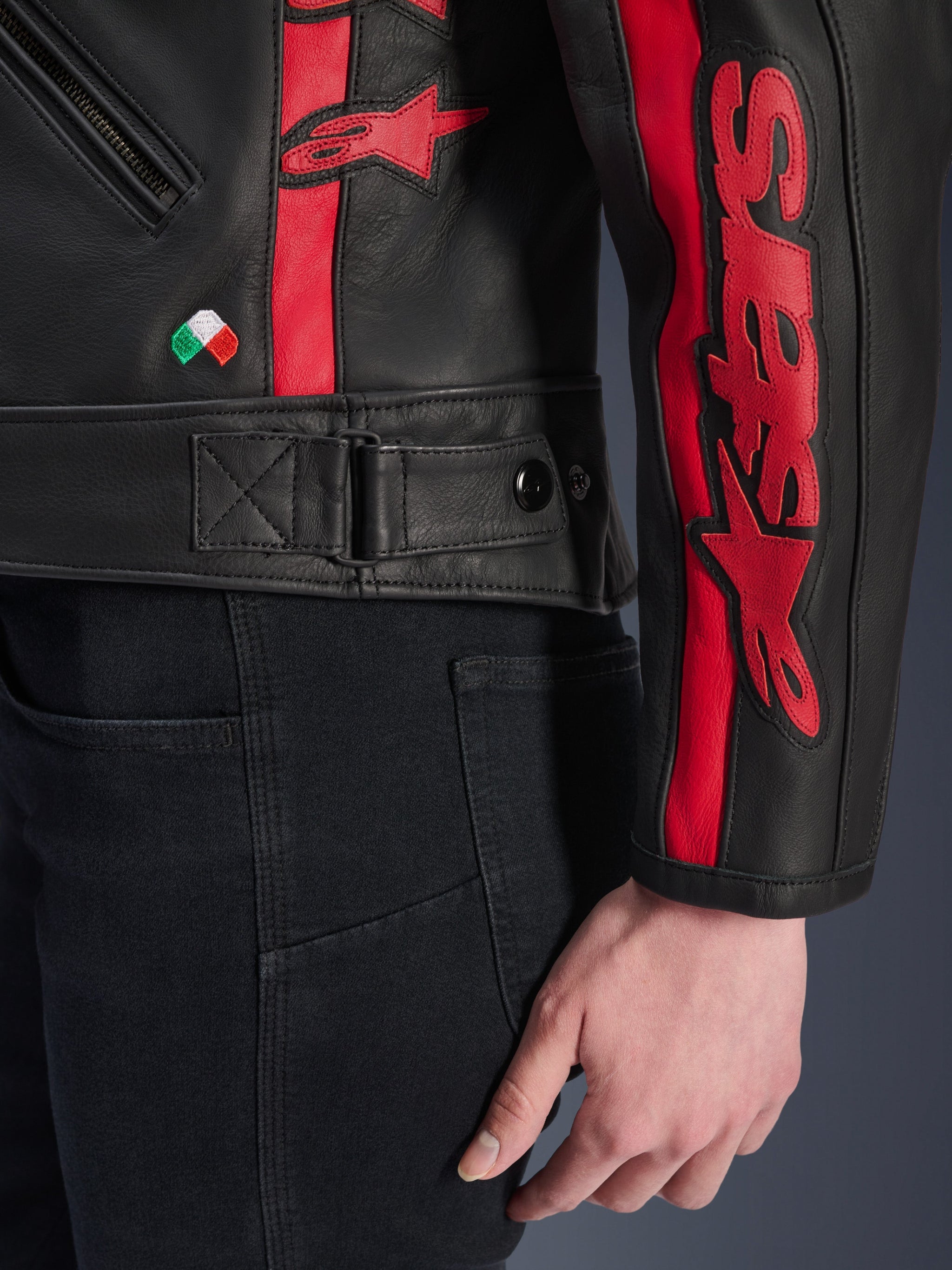 Alpinestars Stella Dyno Leather Jacket, Women's Leather Motorcycle Jacket, Black Haute Red, close-up view of waist and sleeve, red racing stripes with Alpinestars branding, adjustable waist strap, small Italian flag embroidery, premium bovine leather construction