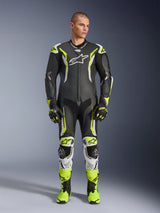 Alpinestars GP Tech V5 One Piece Leather Suit, professional motorcycle racing suit in black and neon yellow fluo with white accents, worn by a model with matching racing gloves and boots, featuring an aerodynamic design and protective sliders.