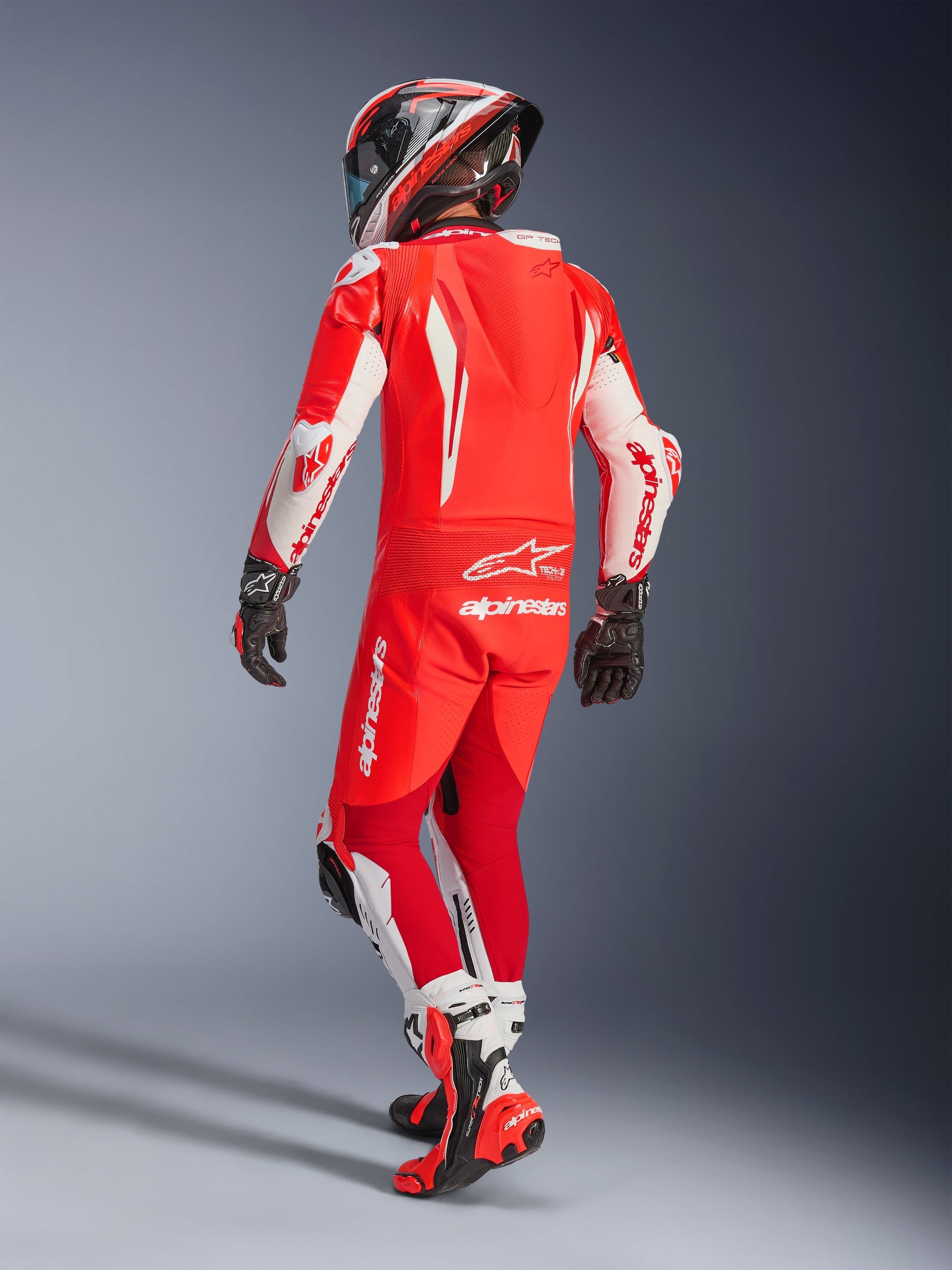 Alpinestars GP Tech V5 One Piece Leather Suit, Red Fluo Bright Red and White, rear view of a motorcyclist in full racing gear, featuring an aerodynamic hump and white panels on sleeves and legs, paired with a matching helmet and red racing boots, professional track performance design.