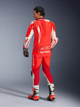 Alpinestars GP Tech V5 One Piece Leather Suit, Red Fluo Bright Red and White, back view showing aerodynamic hump and Alpinestars branding, worn with black racing gloves and white and red racing boots, professional motorcycle racing gear