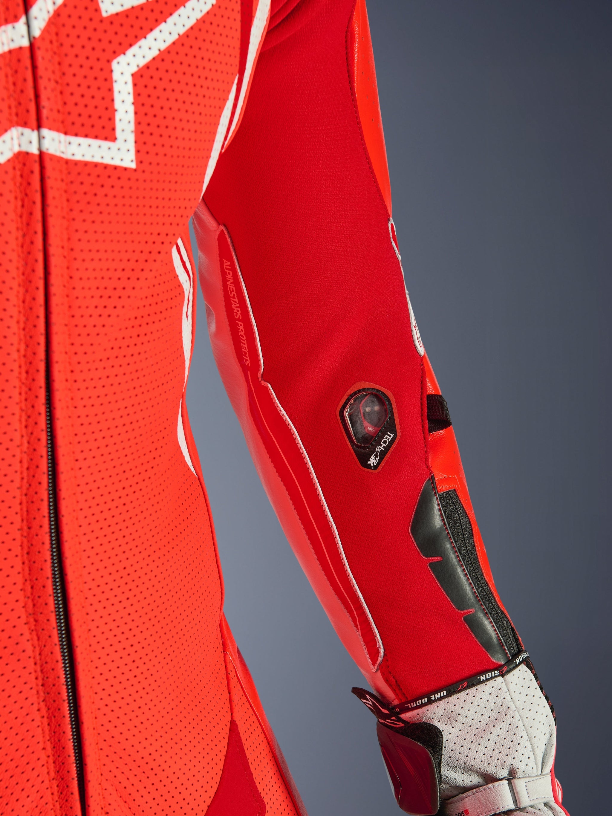Alpinestars GP Tech V5 One Piece Leather Suit, Red Fluo and Bright Red, close-up of the sleeve featuring Tech-Air indicator and protective sliders, perforated leather with white accents, professional racing gear detail