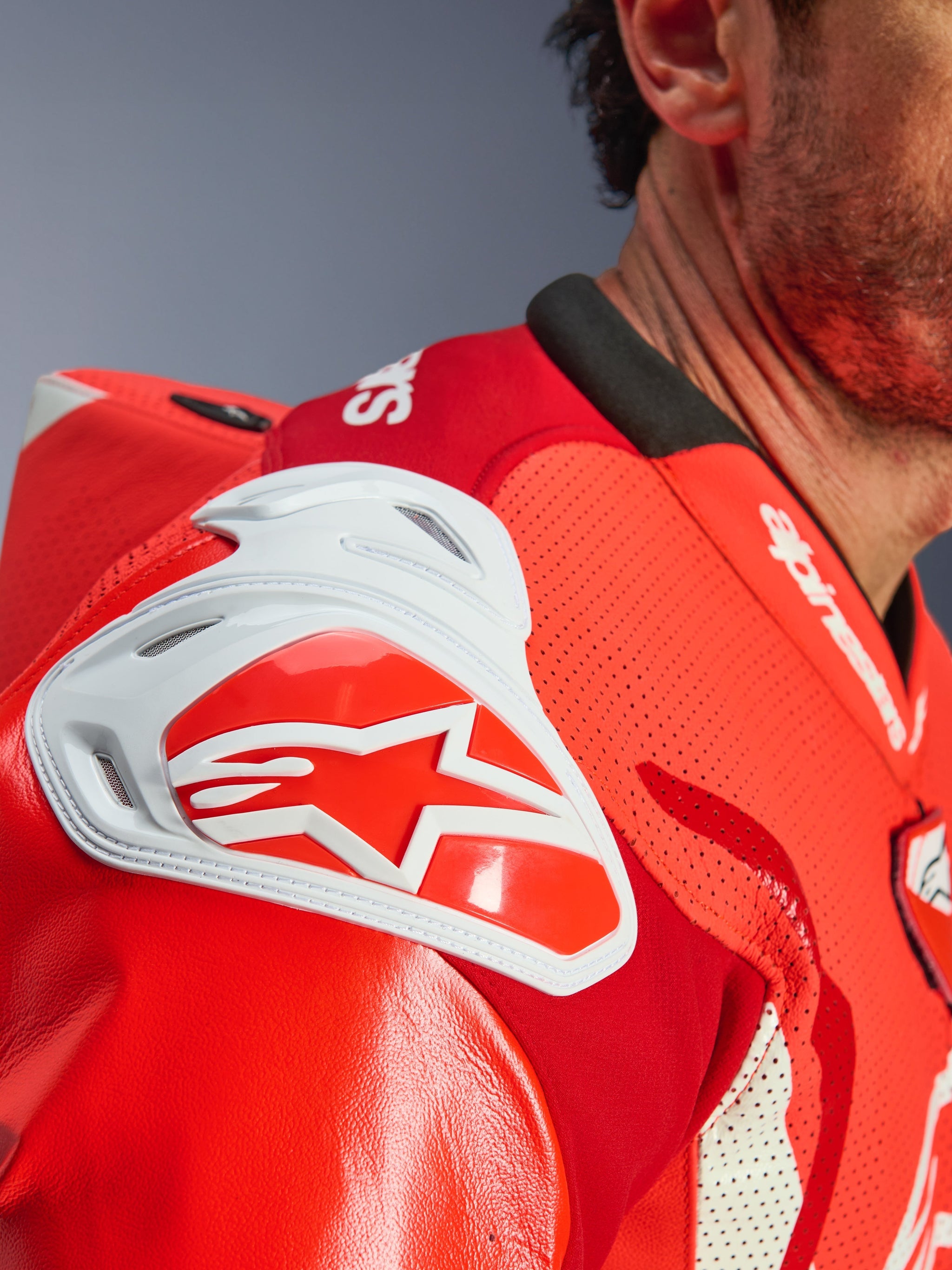 Close-up of the shoulder area on the Alpinestars GP Tech V5 One Piece Leather Suit, Red Fluo and Bright Red, featuring a white GP DFS impact shield with a red star logo and perforated leather for ventilation.