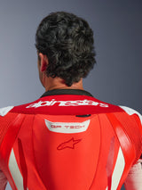 Close-up of the upper back and neck of the GP Tech V5 One Piece Leather Suit, Red Fluo and Bright Red, featuring white Alpinestars wordmark on the collar and GP TECH logo on the aerodynamic hump, worn by a rider.