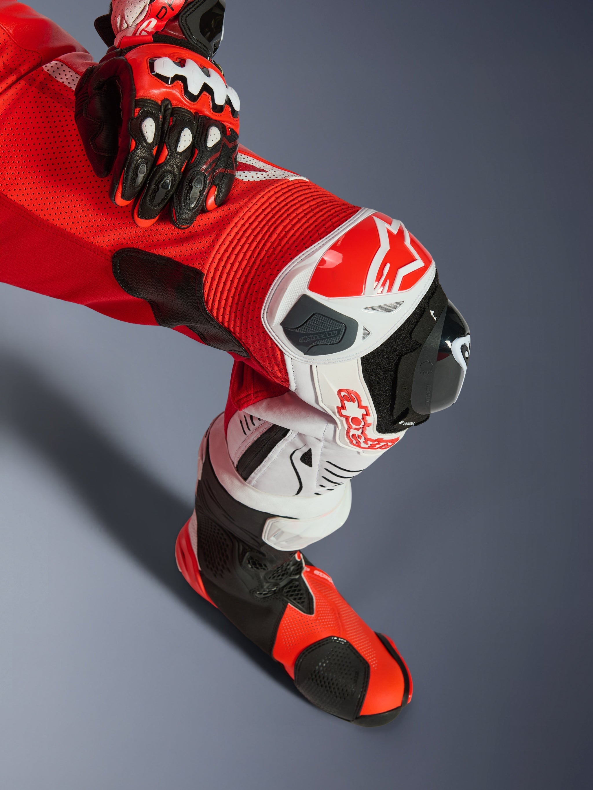 Alpinestars GP Tech V5 One Piece Leather Suit, Red Fluo Bright Red White, close-up of leg showing knee protection and slider, featuring perforated leather and accordion stretch panels, paired with matching racing glove and boot