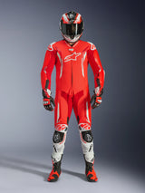 Rider wearing the Alpinestars GP Tech V5 One Piece Leather Suit in Red Fluo, Bright Red, and White, complete with a matching racing helmet, gloves, and boots. Professional track suit featuring an aerodynamic silhouette, white Alpinestars logos, and integrated protective sliders.