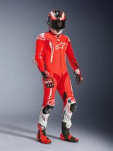 Motorcycle rider wearing the Alpinestars GP Tech V5 One Piece Leather Suit, Red Fluo and Bright Red with White accents, featuring matching helmet, gloves, and racing boots, professional track gear with perforated leather and protective sliders
