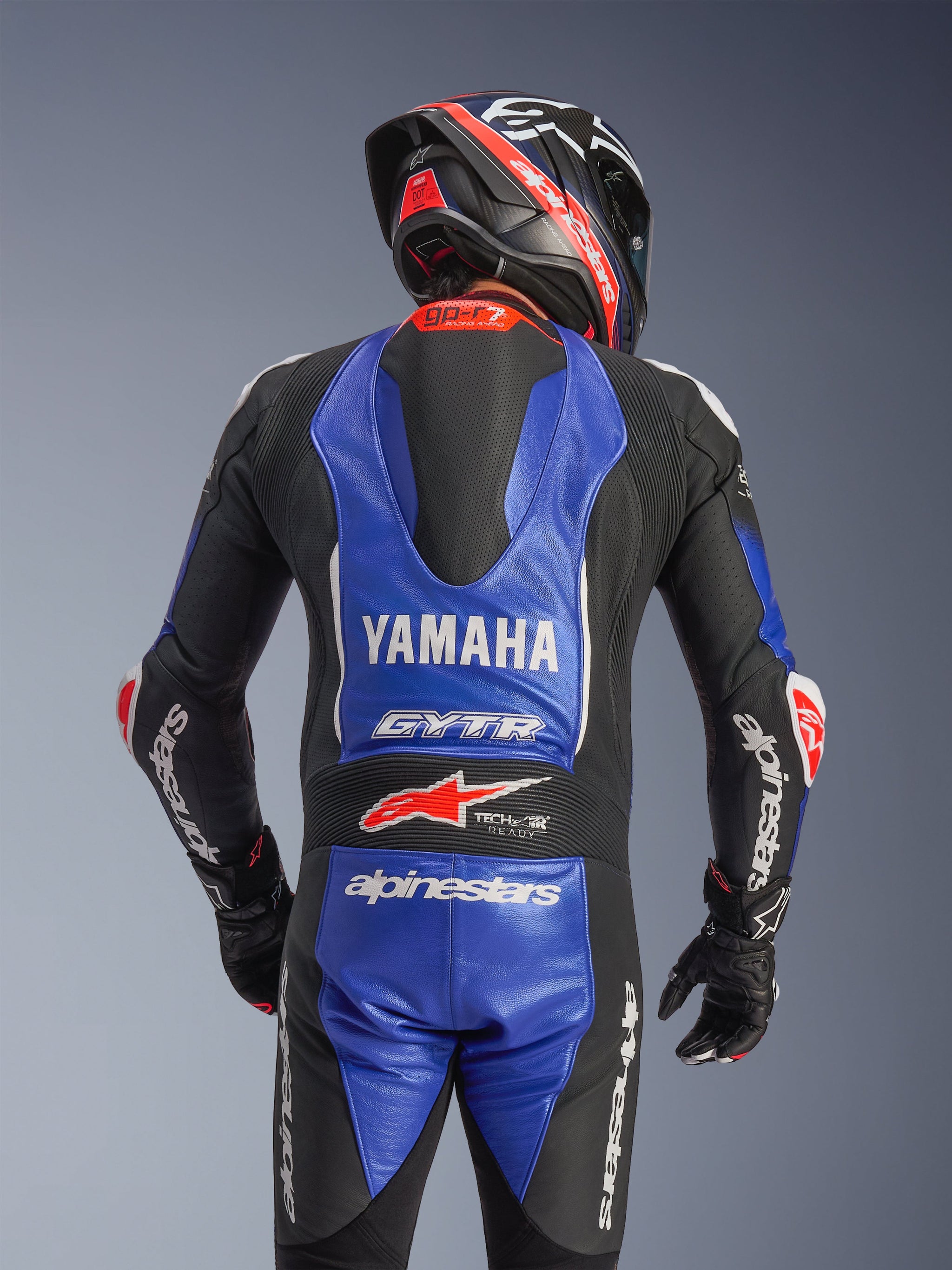 Alpinestars Yamaha GP-R7 One Piece Leather Suit, rear view, Metallic Blue and Black with white and red accents, prominent Yamaha and GYTR branding, featuring an aerodynamic speed hump, worn with a matching racing helmet and gloves for a professional track-ready look
