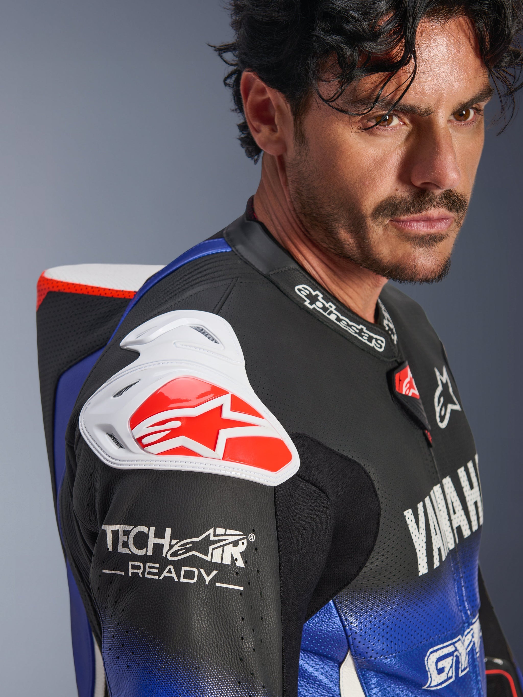 Yamaha GP-R7 One Piece Leather Suit, Metallic Blue Black White and Red, close-up view of the shoulder and chest, featuring white DFS shoulder armor with a red logo, aerodynamic hump, and Tech-Air Ready branding on the perforated leather sleeve.