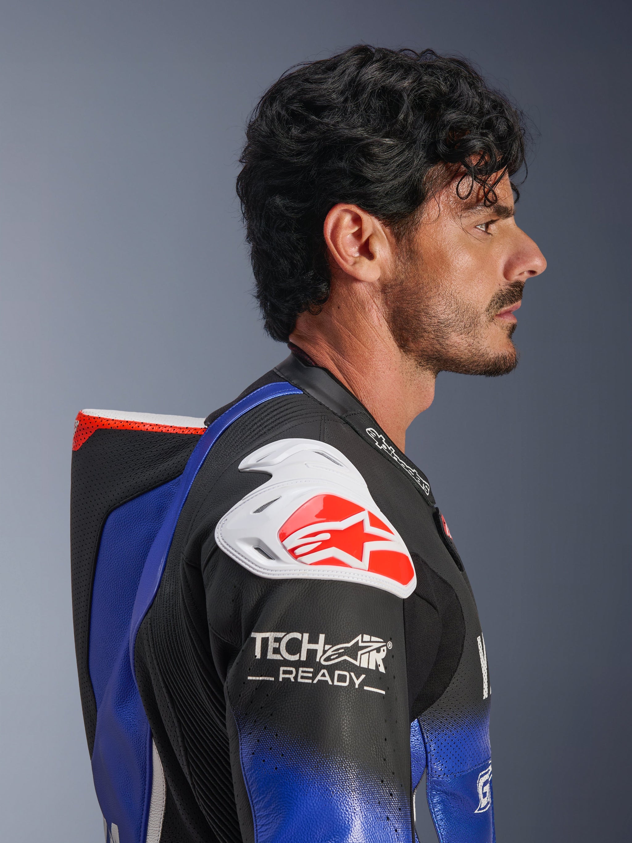 Alpinestars Yamaha GP-R7 One Piece Leather Suit, Metallic Blue and Black with White and Red accents, side profile highlighting the aerodynamic speed hump and white shoulder armor with red Alpinestars logo, Tech-Air Ready branding on the sleeve, premium perforated race leather.