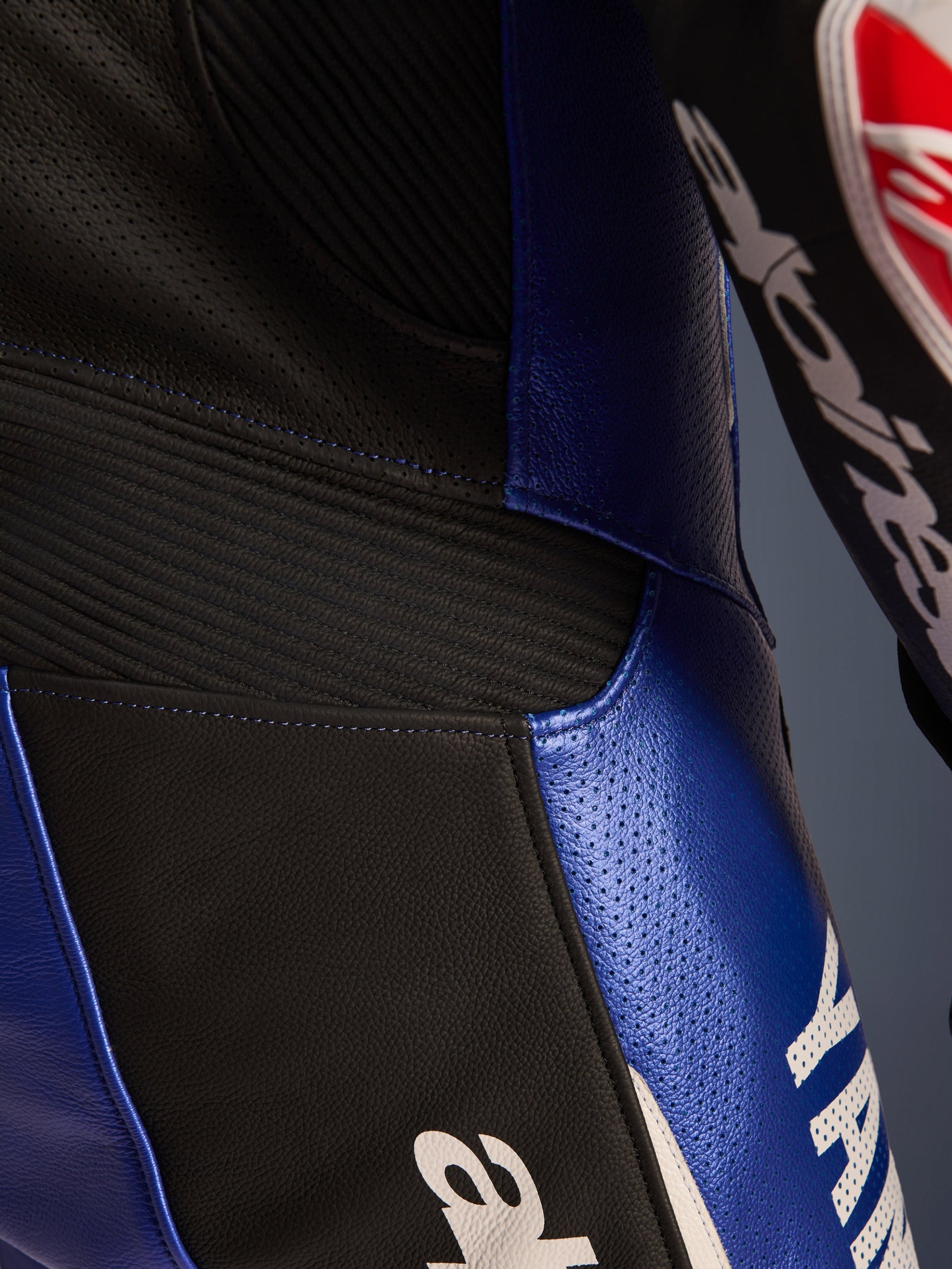 Close-up detail of the Alpinestars Yamaha GP-R7 One Piece Leather Suit, Metallic Blue and Black, featuring perforated leather panels for ventilation, black accordion stretch inserts for flexibility, and bold white Yamaha branding, highlighting the race-grade bovine leather construction.