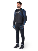 Alpinestars T-Jaws V4 Waterproof Jacket in Black, Dark Blue, and Blithe Blue, worn by a model with black motorcycle pants and riding boots, featuring white Alpinestars logo on chest and blue shoulder accents, sport-fit riding gear.