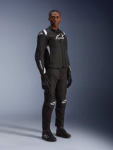 Male model wearing Alpinestars T-SP 1 V2 Waterproof Jacket in Black and White, styled with matching black motorcycle pants, gloves, and boots. Full-body studio shot featuring a sport textile jacket with white logos and a 3D tailored silhouette.