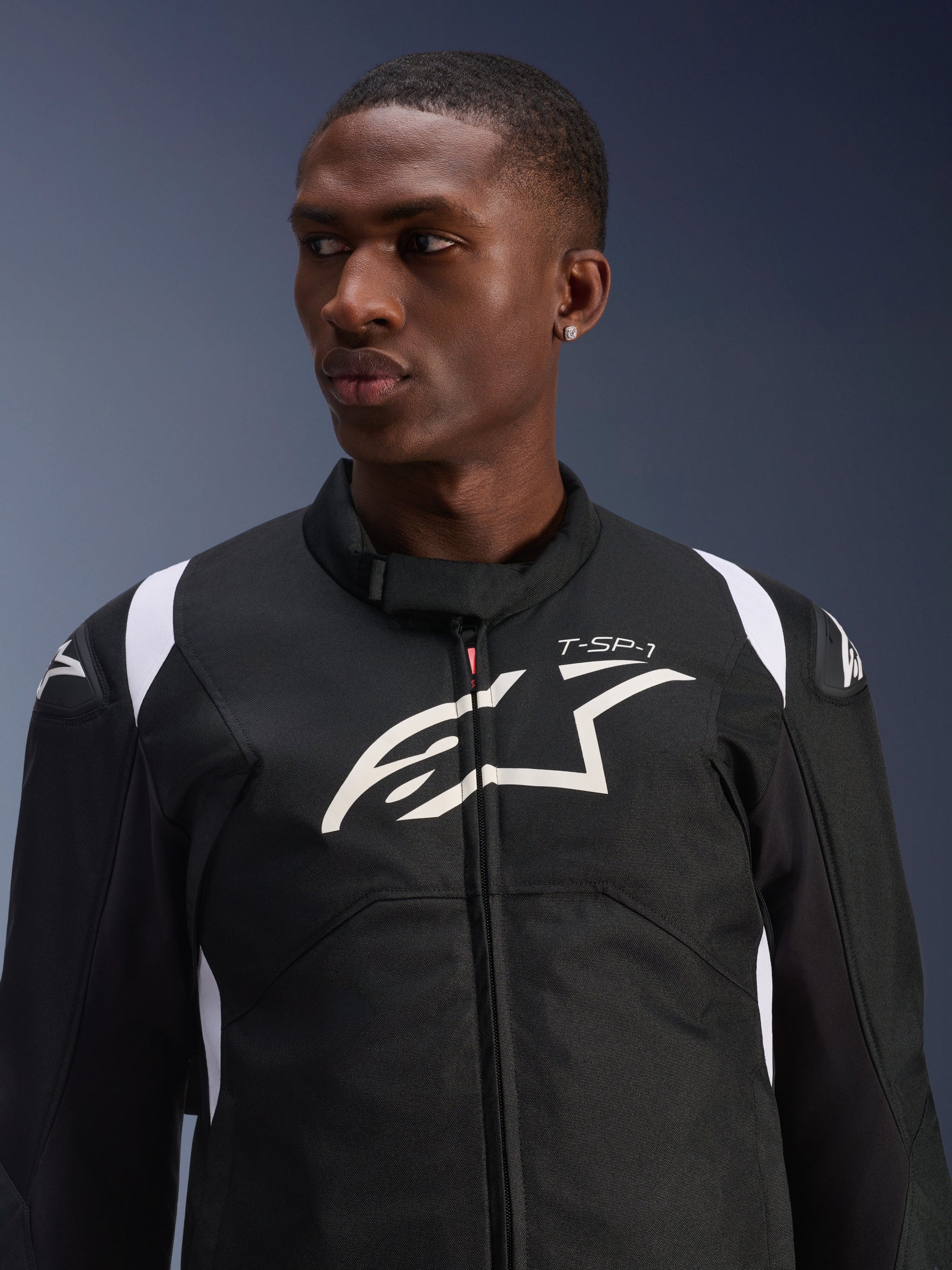 Alpinestars T-SP 1 V2 Waterproof Jacket worn by a model, black and white textile motorcycle jacket, large white Alpinestars logo and T-SP-1 branding on the chest, sporty design with protective shoulder sliders