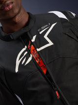 Alpinestars T-SP 1 V2 Waterproof Jacket, Black and White, featuring a large white chest logo and 'T-SP-1' text, orange internal flap with 'Alpinestars Protects' and 'Tech-Air Ready' branding, durable textile motorcycle gear