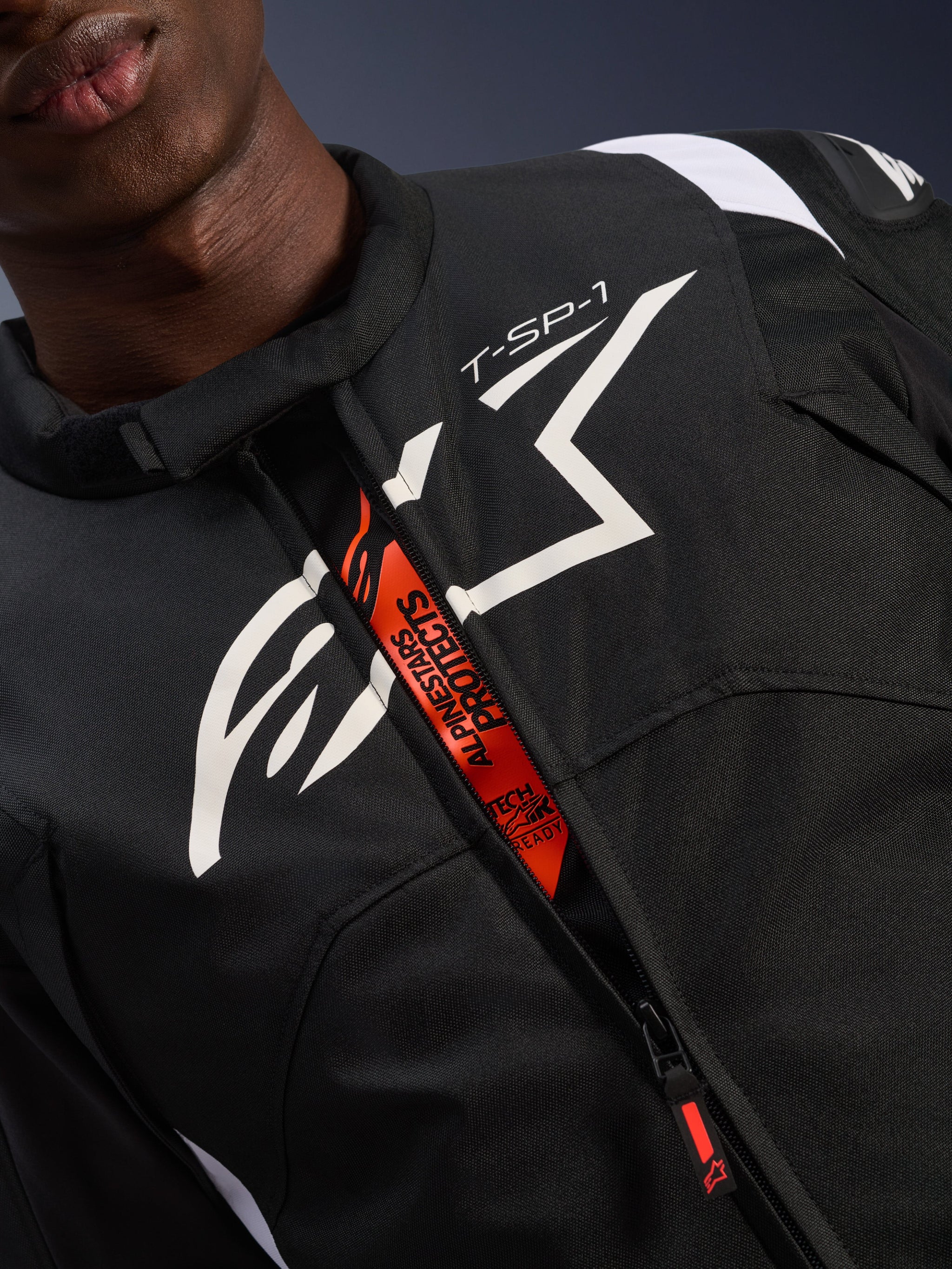 Alpinestars T-SP 1 V2 Waterproof Jacket, Black and White, featuring a large white chest logo and 'T-SP-1' text, orange internal flap with 'Alpinestars Protects' and 'Tech-Air Ready' branding, durable textile motorcycle gear