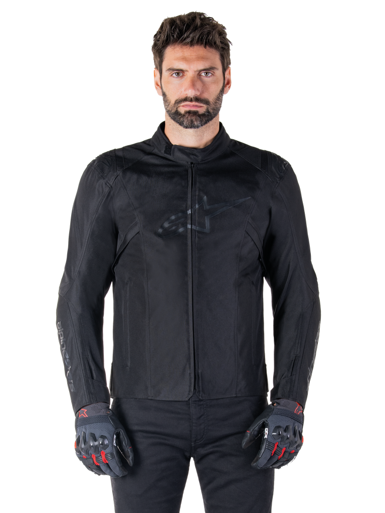 Alpinestars T-SPS V2 Waterproof Jacket, Black motorcycle textile jacket, worn by rider with black and red gloves, featuring a high collar, zippered front, and subtle chest logo, waterproof protection for sport and urban riding