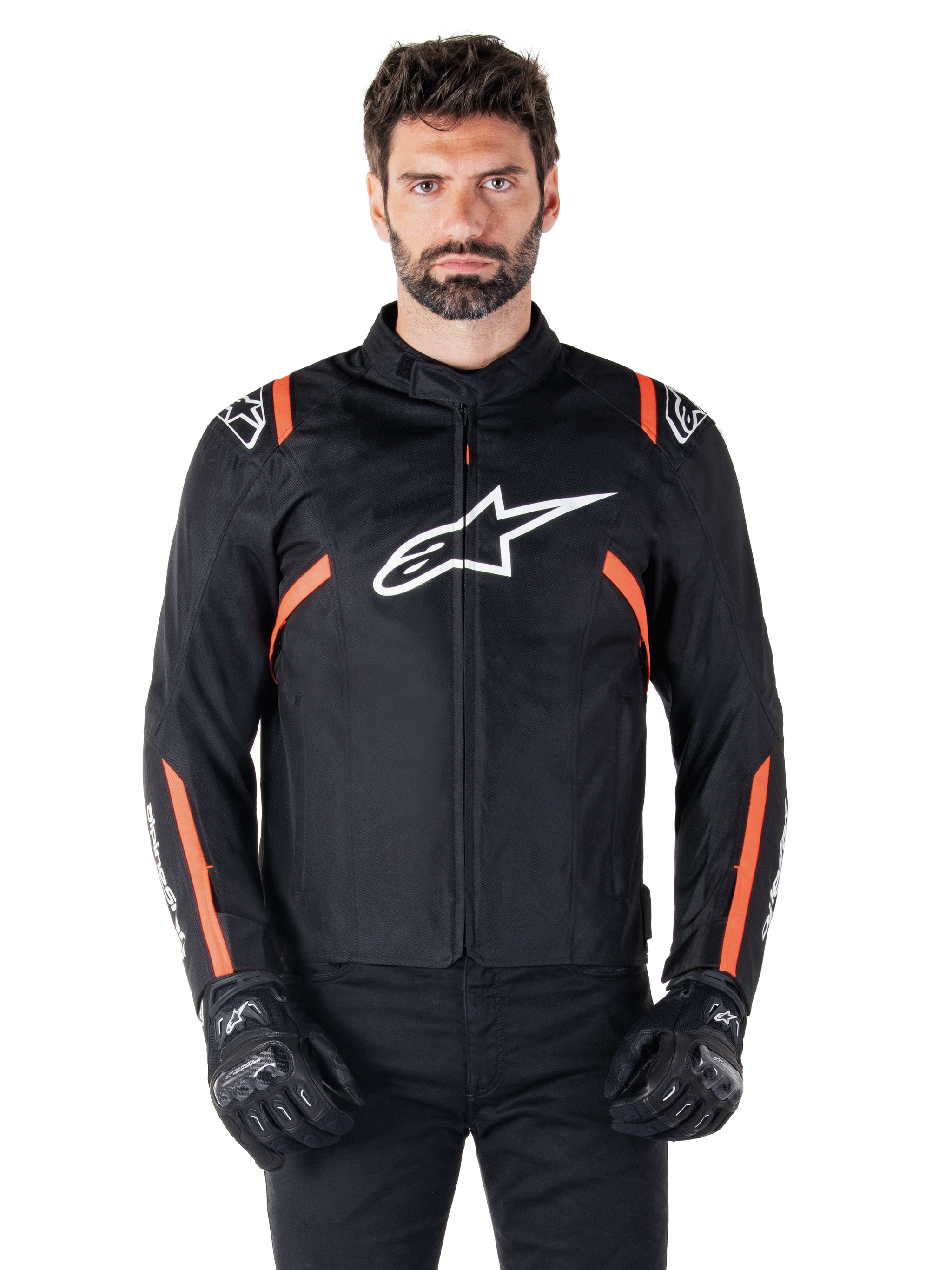 Alpinestars T-SPS V2 Waterproof Jacket, Black White and Red Fluo, worn by a male model with black riding gloves, featuring a large white Alpinestars logo on the chest and vibrant orange accents on the shoulders and sleeves.