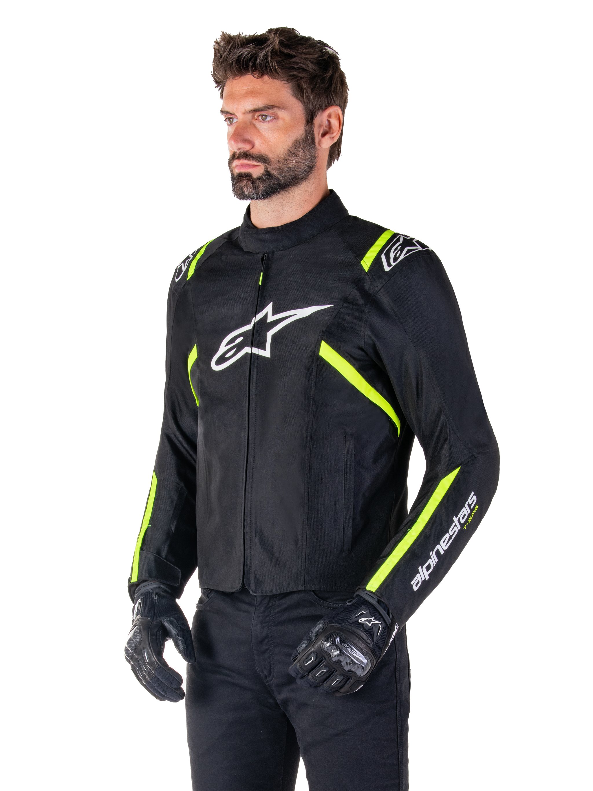 Male model wearing the Alpinestars T-SPS V2 Waterproof Jacket, Black with White and Yellow Fluo accents, featuring a white Astars logo on the chest and fluorescent yellow stripes on the shoulders and sleeves, paired with black pants and riding gloves, sport-cut textile motorcycle jacket.