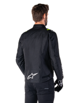 Alpinestars T-SPS V2 Waterproof Jacket, Black White Yellow Fluo, rear view of male model wearing the textile motorcycle jacket, featuring a white logo on the lower back and yellow fluo accents on the shoulders, paired with black pants and gloves.