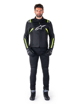 Alpinestars T-SPS V2 Waterproof Jacket, Black White and Yellow Fluo, worn by a model with black riding pants and gloves, featuring a white Alpinestars logo on the chest and fluorescent accents on shoulders and sleeves, sport-cut motorcycle gear
