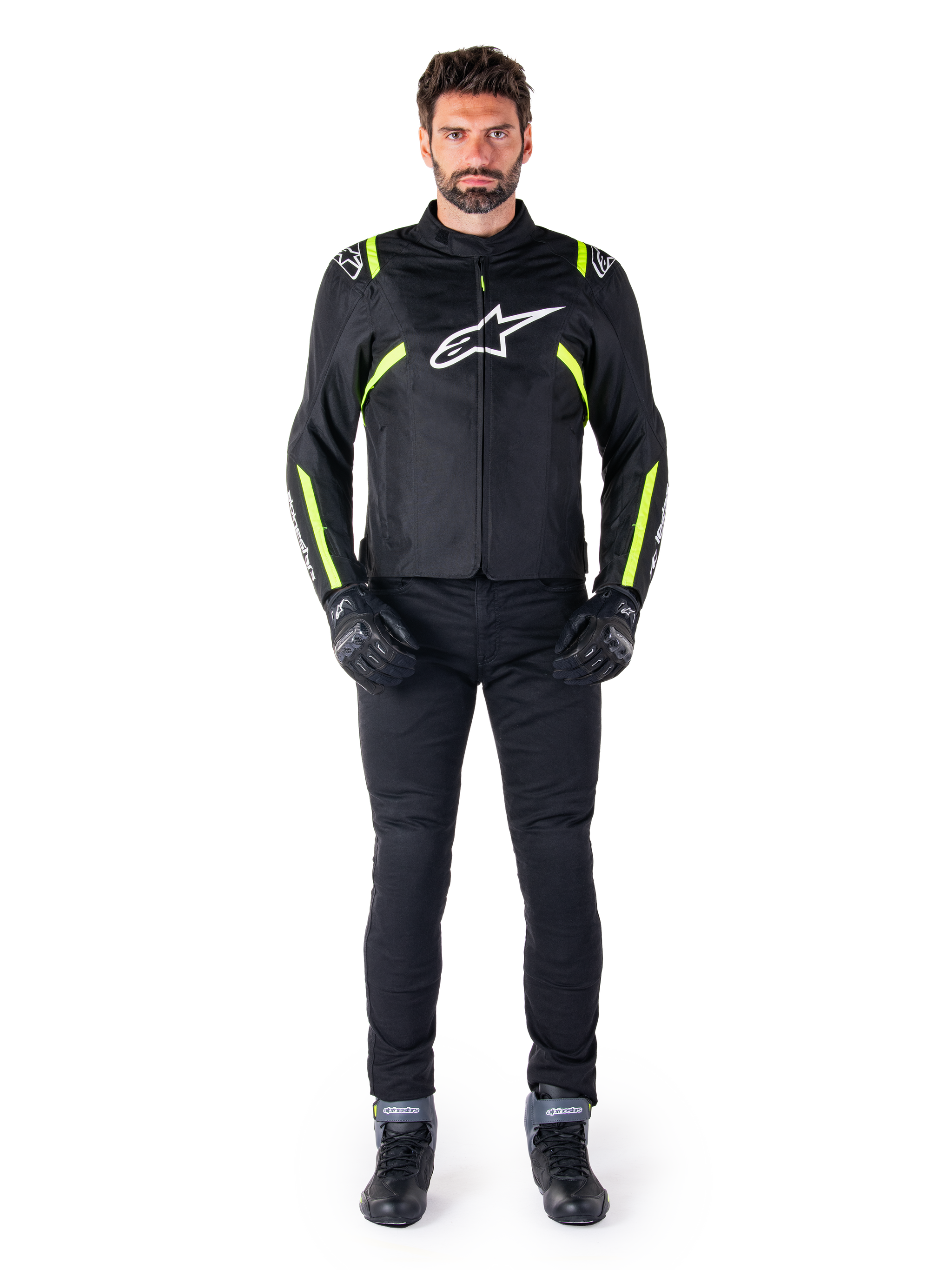 Alpinestars T-SPS V2 Waterproof Jacket, Black White and Yellow Fluo, worn by a model with black riding pants and gloves, featuring a white Alpinestars logo on the chest and fluorescent accents on shoulders and sleeves, sport-cut motorcycle gear