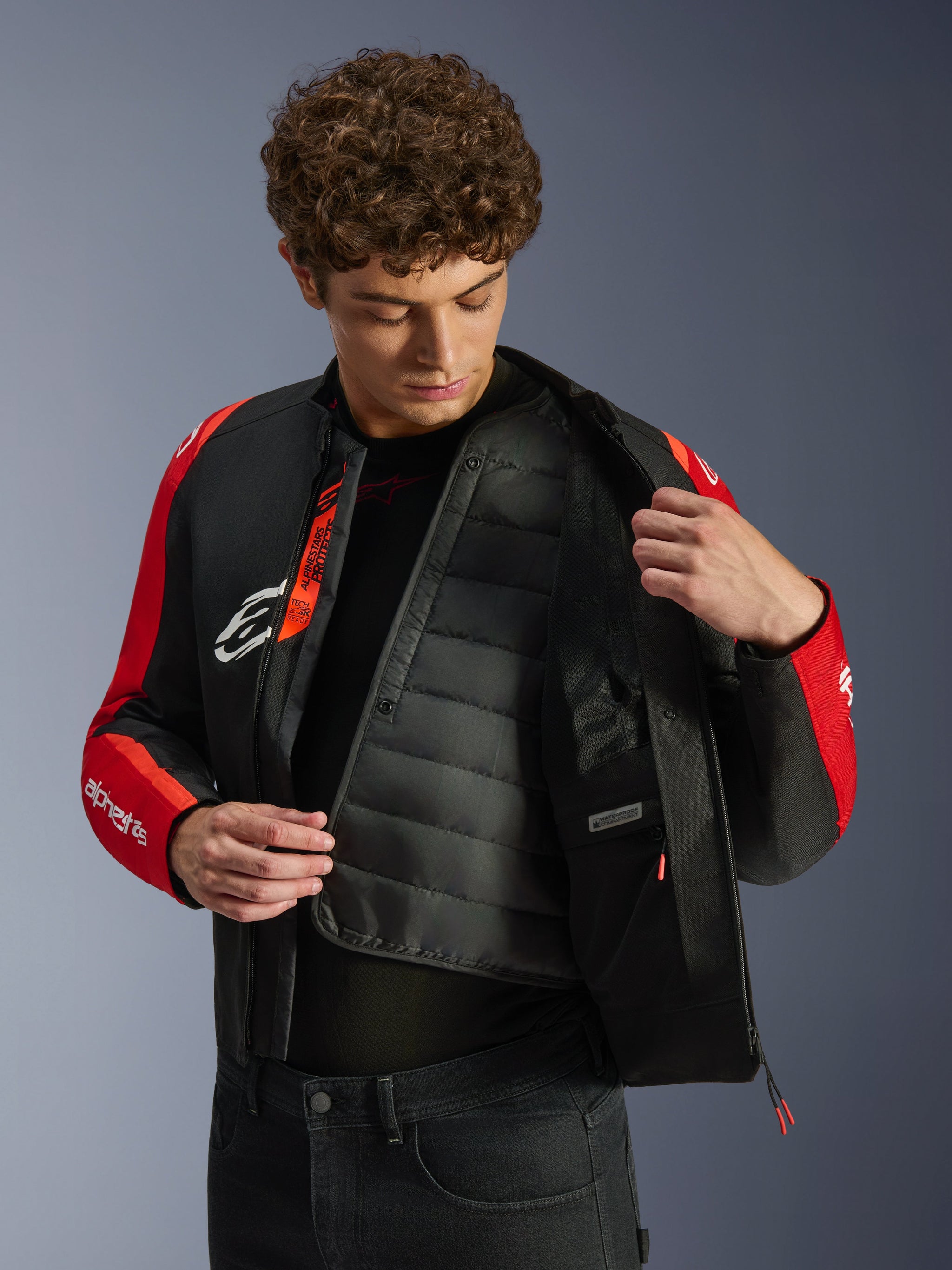 Alpinestars T-SPS V2 Waterproof Jacket, Black and Red, featuring a model revealing the internal quilted thermal liner and waterproof compartment, Tech-Air Ready branding on the interior, sport-cut motorcycle jacket.