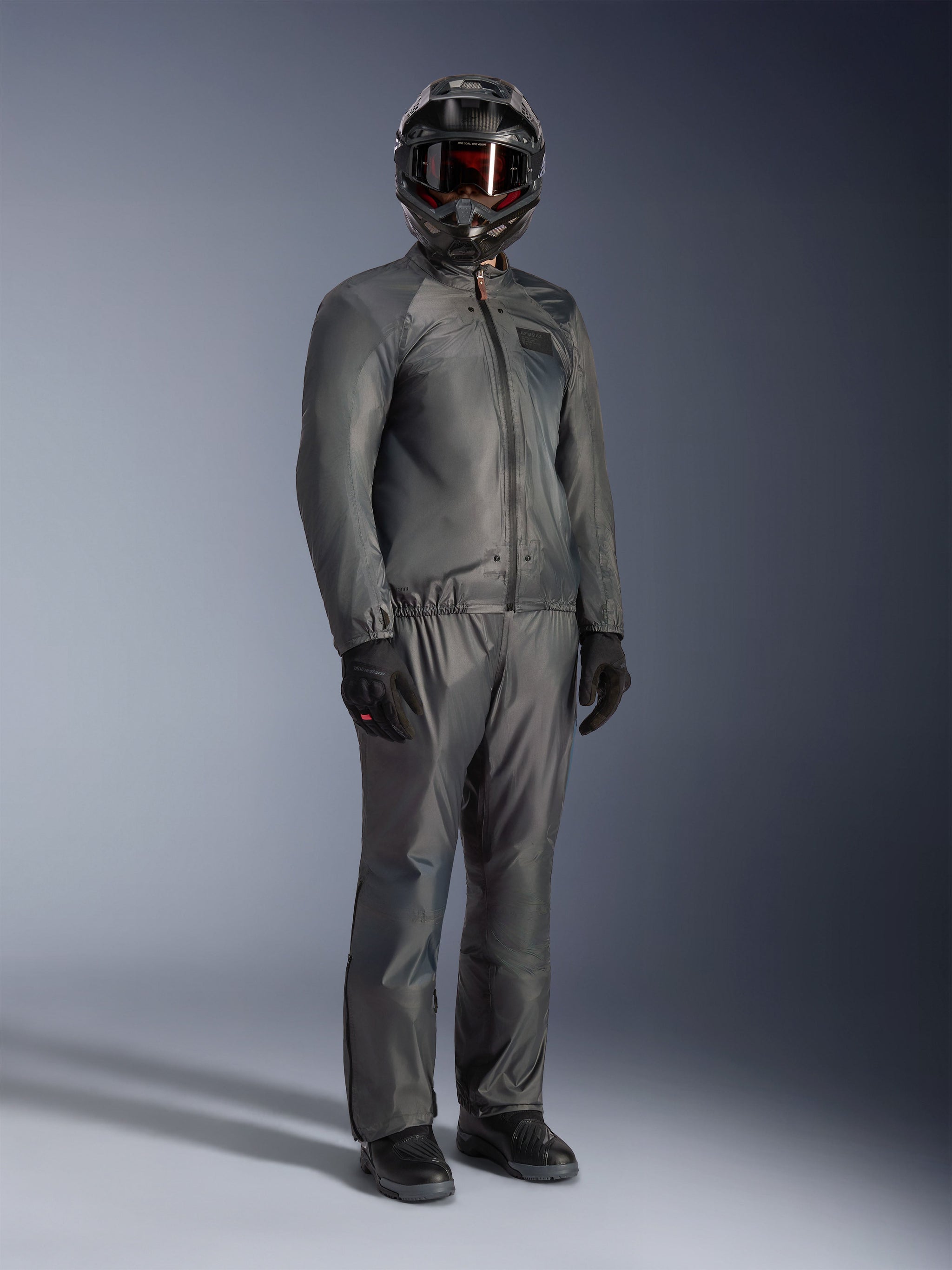 Rider wearing the Alpinestars Borrego Drystar® Jacket in Warm Gray, full-body adventure gear with matching gray pants, black full-face helmet with goggles, and black gloves, featuring a sleek waterproof textile design.