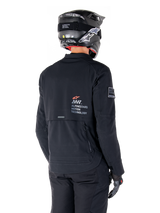 Rear view of a rider wearing the Alpinestars AMT-8 Stretch Drystar® XF Jacket in Black, featuring 'AMT Alpinestars Motion Technology' branding on the back, technical zippered ventilation, paired with a black motorcycle helmet and gloves