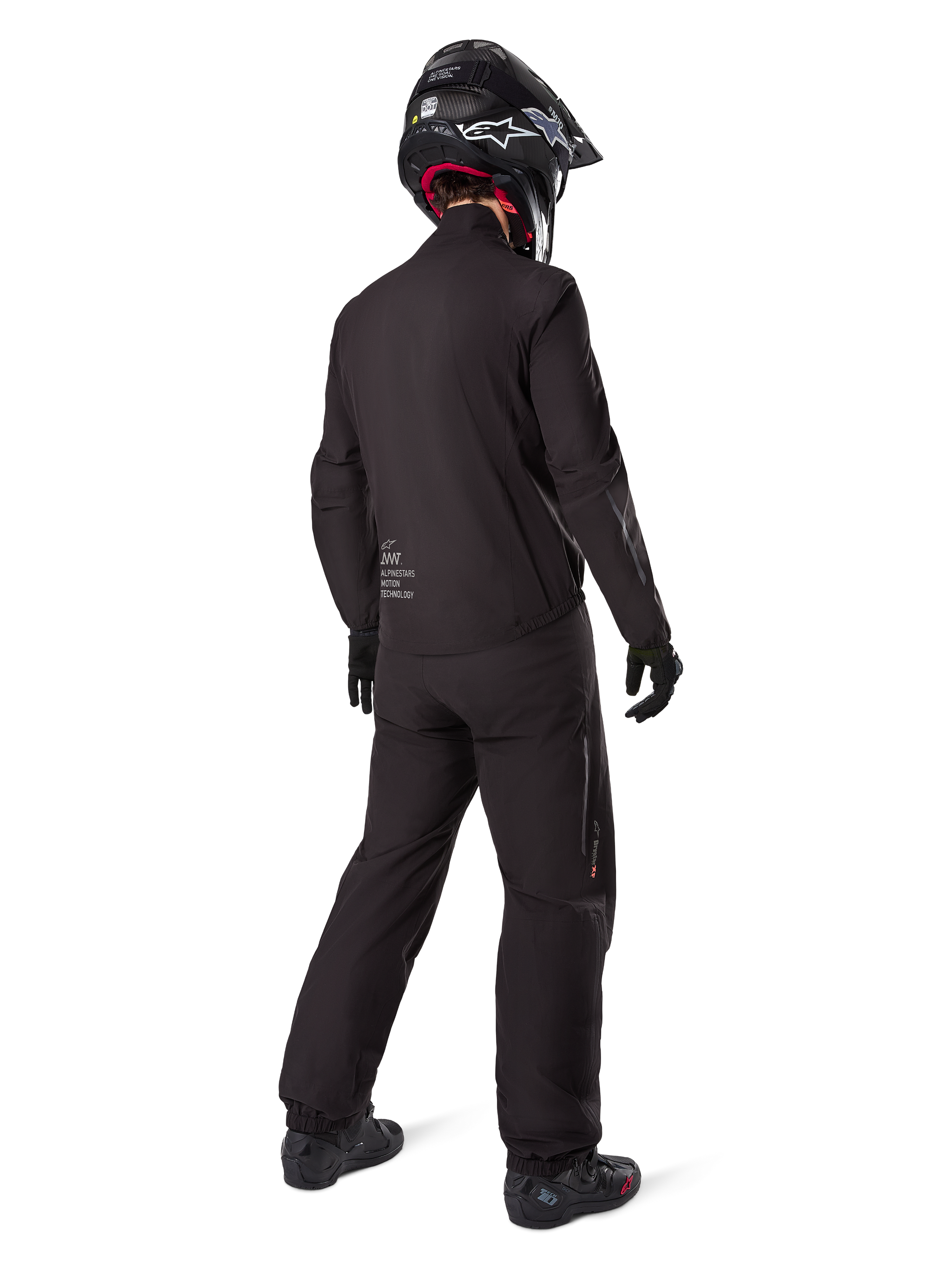 Rear view of a rider wearing the Alpinestars AMT-8 Stretch Drystar® XF Jacket liner, Black technical motorcycle gear, worn with matching pants and black helmet, featuring "AMT Alpinestars Motion Technology" branding on the back, sleek minimalist design for adventure touring