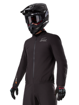 Rider wearing the Alpinestars AMT-8 Stretch Drystar® XF Liner, black windproof and waterproof stretch jacket, featuring AMT logo on the chest and Drystar XF branding on the sleeve, paired with a black adventure helmet and protective gloves.