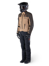 Adventure rider wearing complete gear, Alpinestars AMT-8 Stretch Drystar® XF Jacket in Dark Brown and Dark Khaki, paired with black adventure pants, black helmet, gloves, and boots, featuring orange AMT branding and technical ventilation zippers for long-range touring