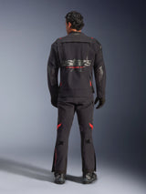A rider seen from behind wearing the Alpinestars Halo Pro Drystar® XF Laminated Jacket in Black Dark Shadow, featuring a large gray astars logo with red Alpinestars branding, modular ventilation panels on the back, and paired with matching adventure riding pants and black boots.